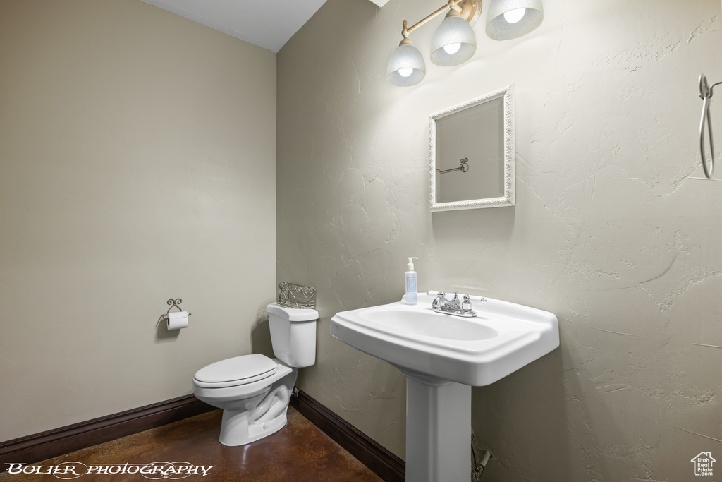 Half bathroom featuring baseboards, toilet, and concrete floors