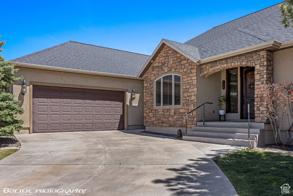 Ranch-style home with an attached garage, roof with shingles, stucco siding, and stone siding
