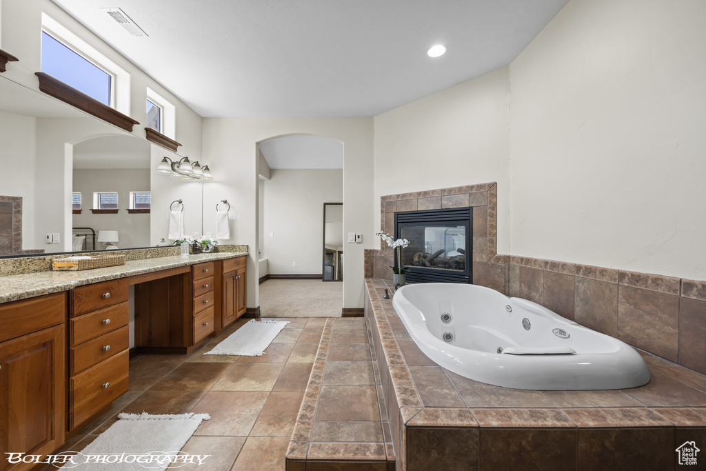 Full bathroom with visible vents, a fireplace, vanity, baseboards, and a whirlpool tub