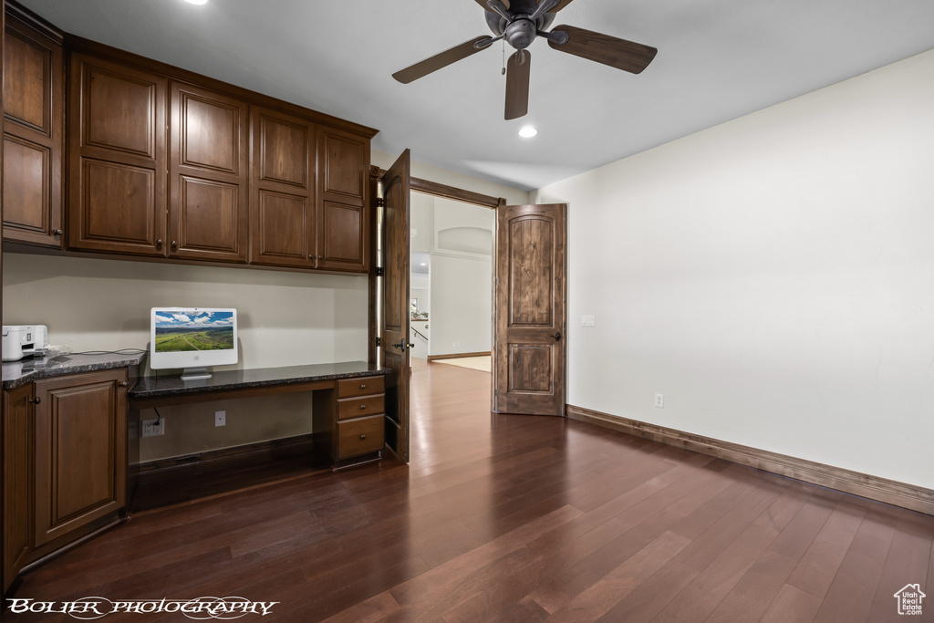 Unfurnished office featuring dark wood-style flooring, built in desk, a ceiling fan, baseboards, and recessed lighting