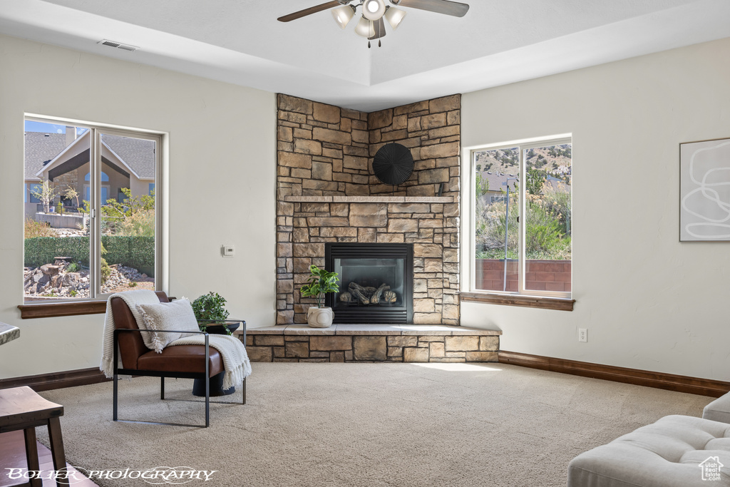 Carpeted living area with visible vents, baseboards, ceiling fan, and a stone fireplace