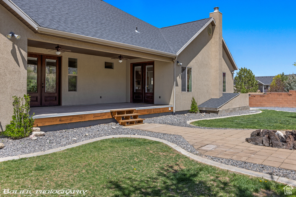 Back of property featuring ceiling fan, french doors, a chimney, a yard, and stucco siding