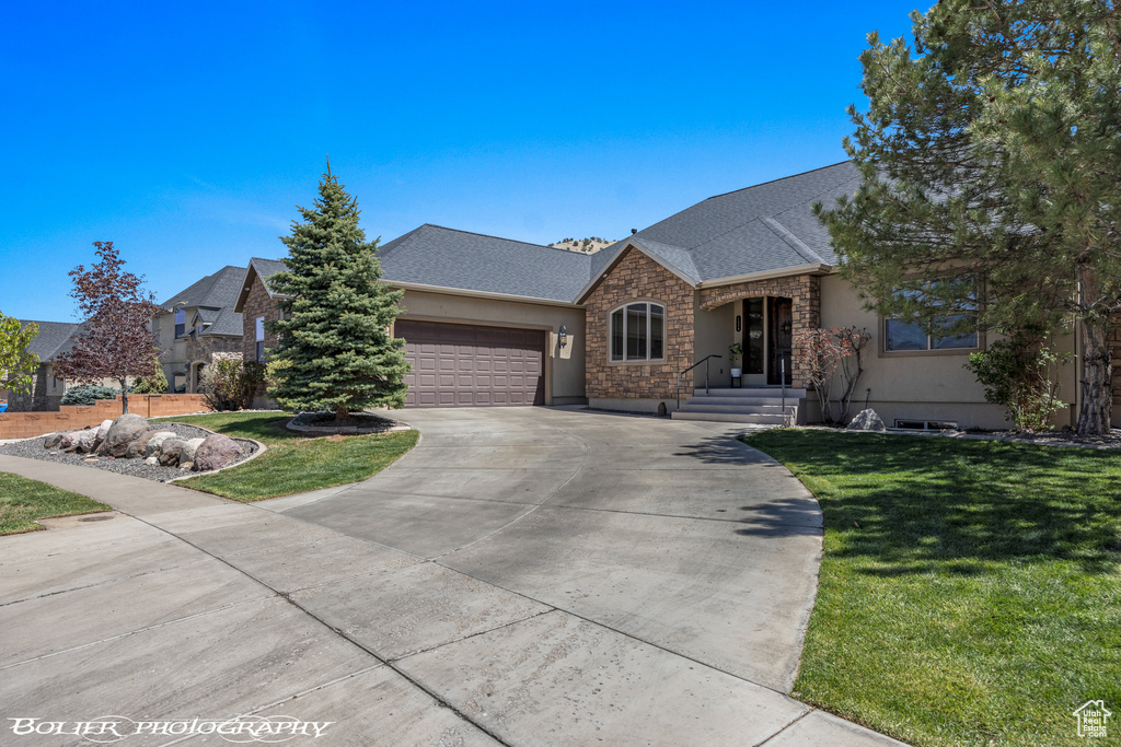 Ranch-style home with a garage, a front yard, stone siding, and concrete driveway