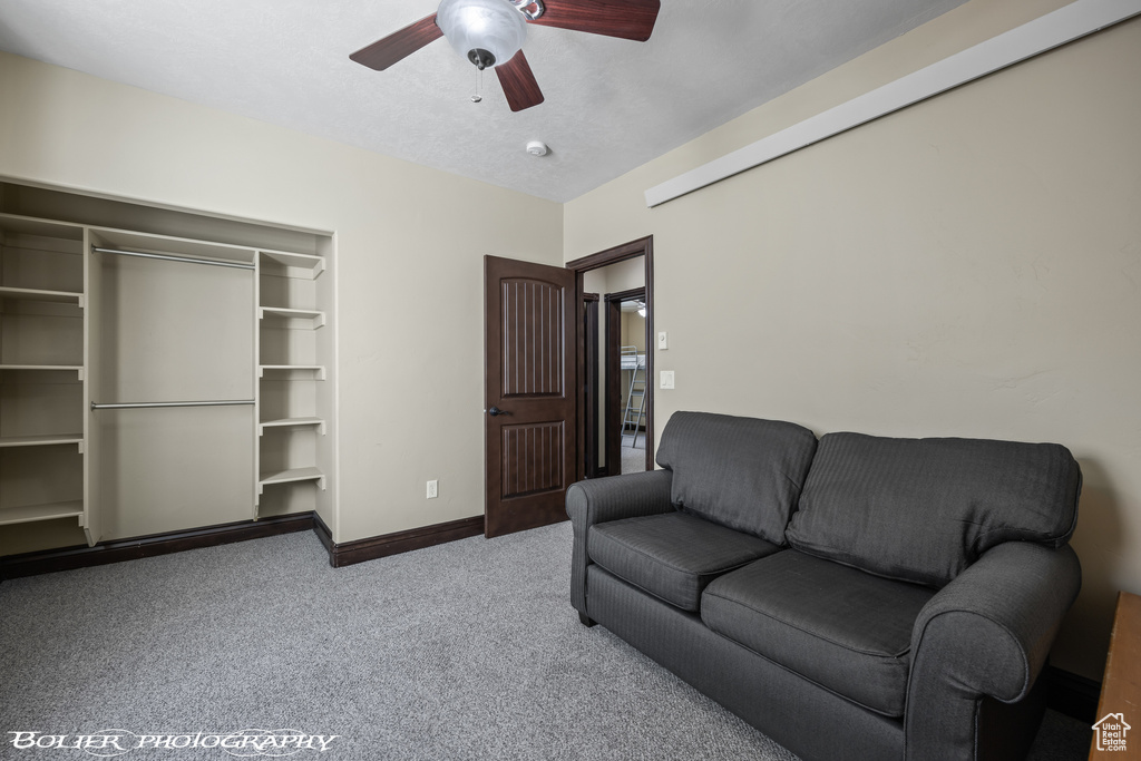 Carpeted living area with a ceiling fan and baseboards