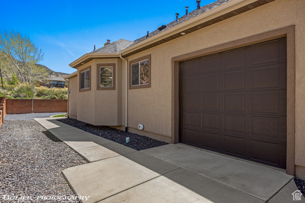 View of property exterior featuring roof with shingles, a garage, fence, a mountain view, and stucco siding