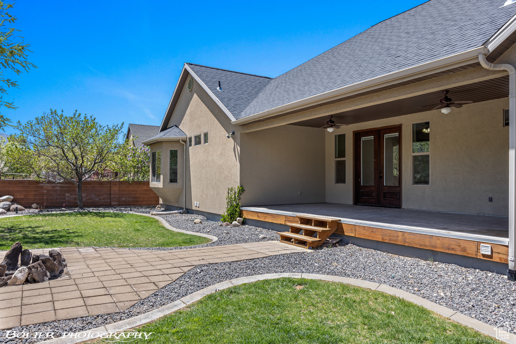 Back of property featuring fence, french doors, stucco siding, a lawn, and a ceiling fan