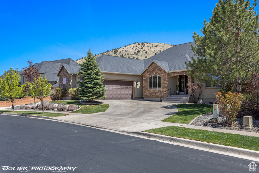 Ranch-style home with a garage, stone siding, stucco siding, a mountain view, and driveway