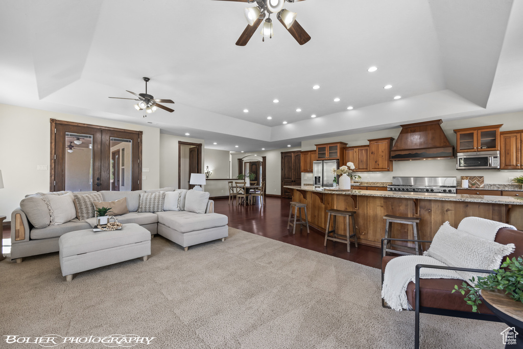 Carpeted living area featuring a raised ceiling, ceiling fan, and recessed lighting
