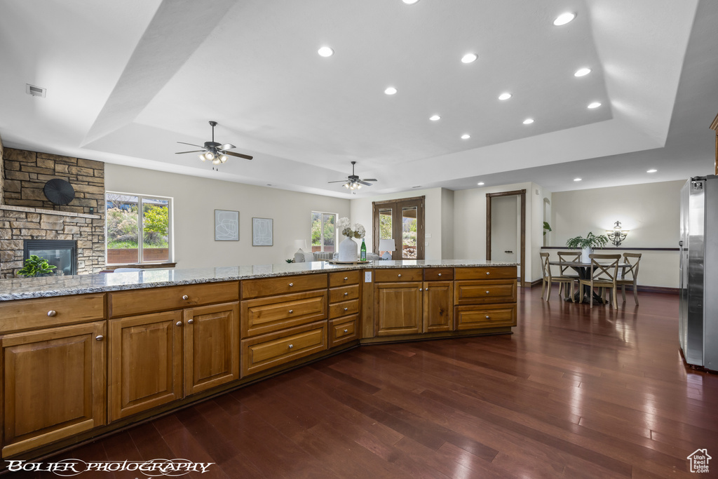 Kitchen featuring brown cabinetry, a ceiling fan, dark wood-style flooring, a raised ceiling, and freestanding refrigerator