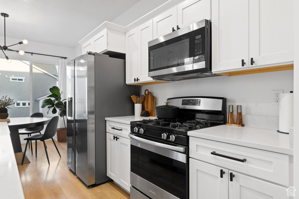 Kitchen with light wood-style floors, white cabinetry, a chandelier, appliances with stainless steel finishes, and hanging light fixtures