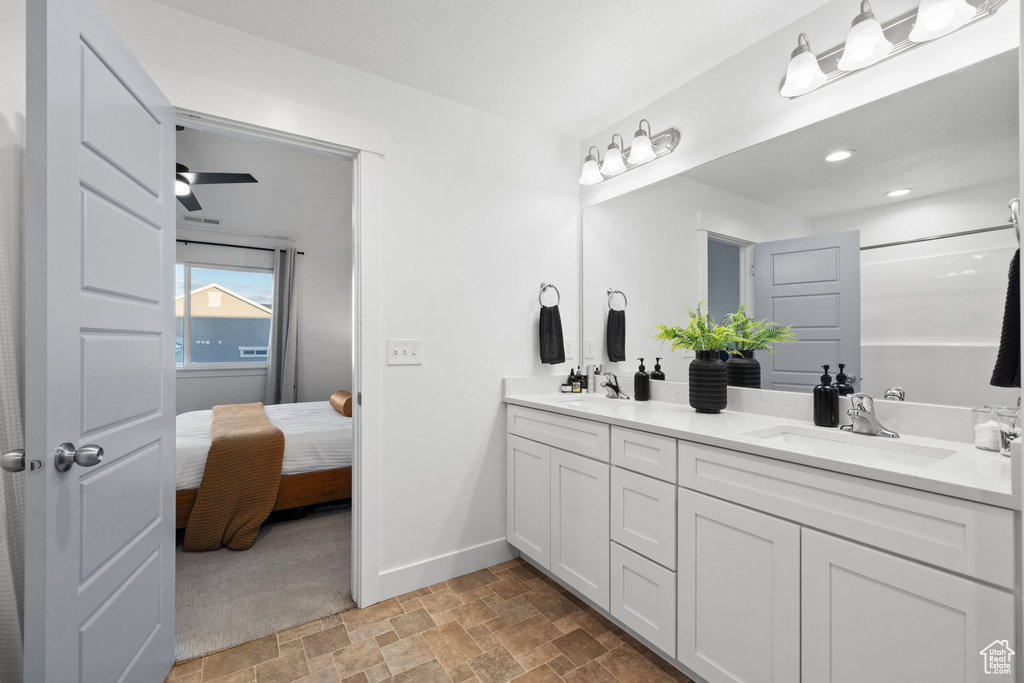 Ensuite bathroom featuring double vanity, baseboards, stone finish floor, and a sink