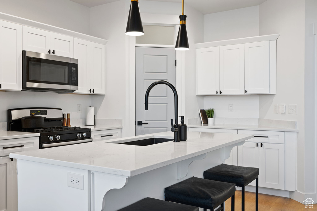 Kitchen with a sink, a kitchen breakfast bar, stainless steel appliances, and white cabinetry