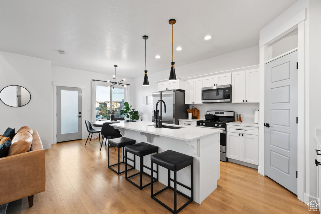 Kitchen with a notable chandelier, appliances with stainless steel finishes, a breakfast bar area, a kitchen island with sink, and recessed lighting