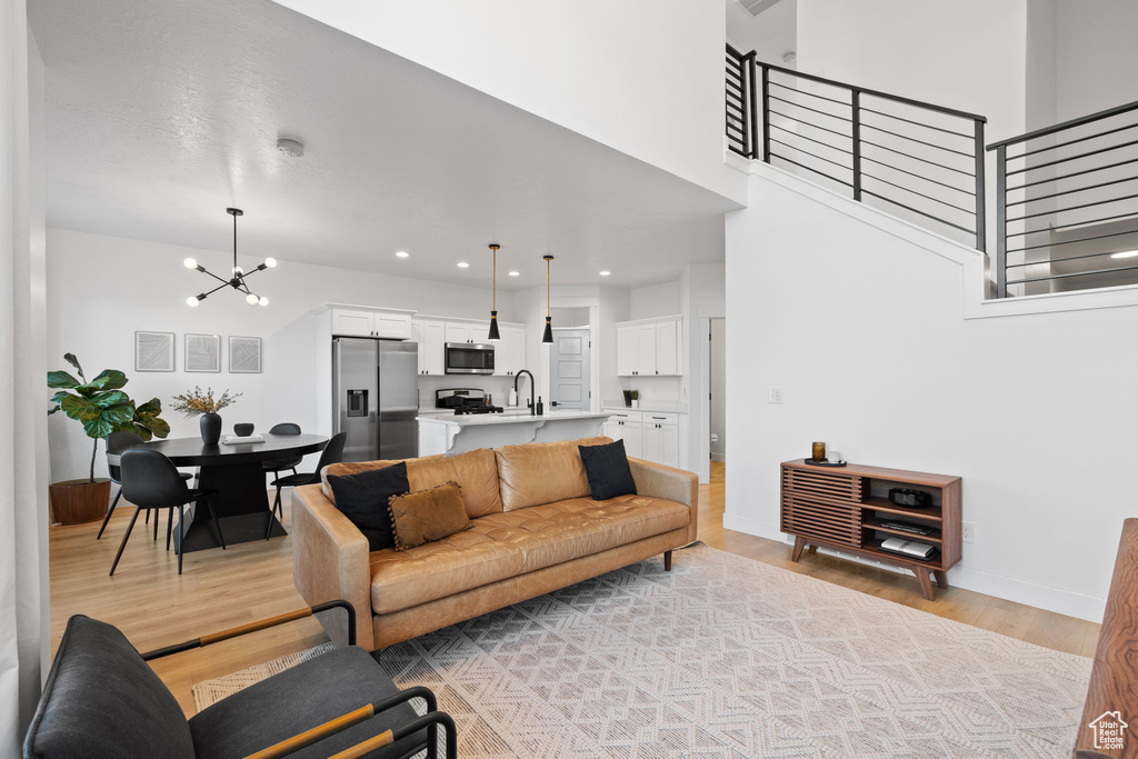 Living area with a high ceiling, light wood-style floors, a chandelier, stairs, and baseboards
