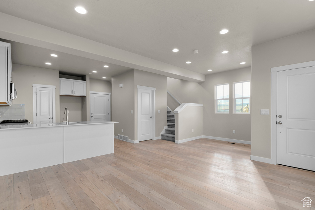 Unfurnished living room with stairs, recessed lighting, a sink, and light wood finished floors