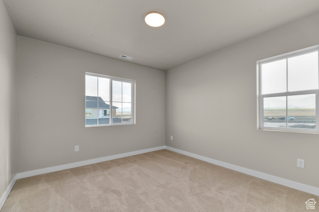 Empty room featuring baseboards, visible vents, and light carpet