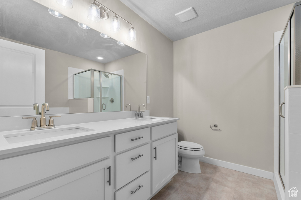 Full bathroom featuring double vanity, a sink, toilet, and a shower stall