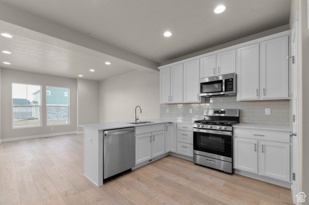 Kitchen with decorative backsplash, appliances with stainless steel finishes, a sink, light countertops, and a peninsula
