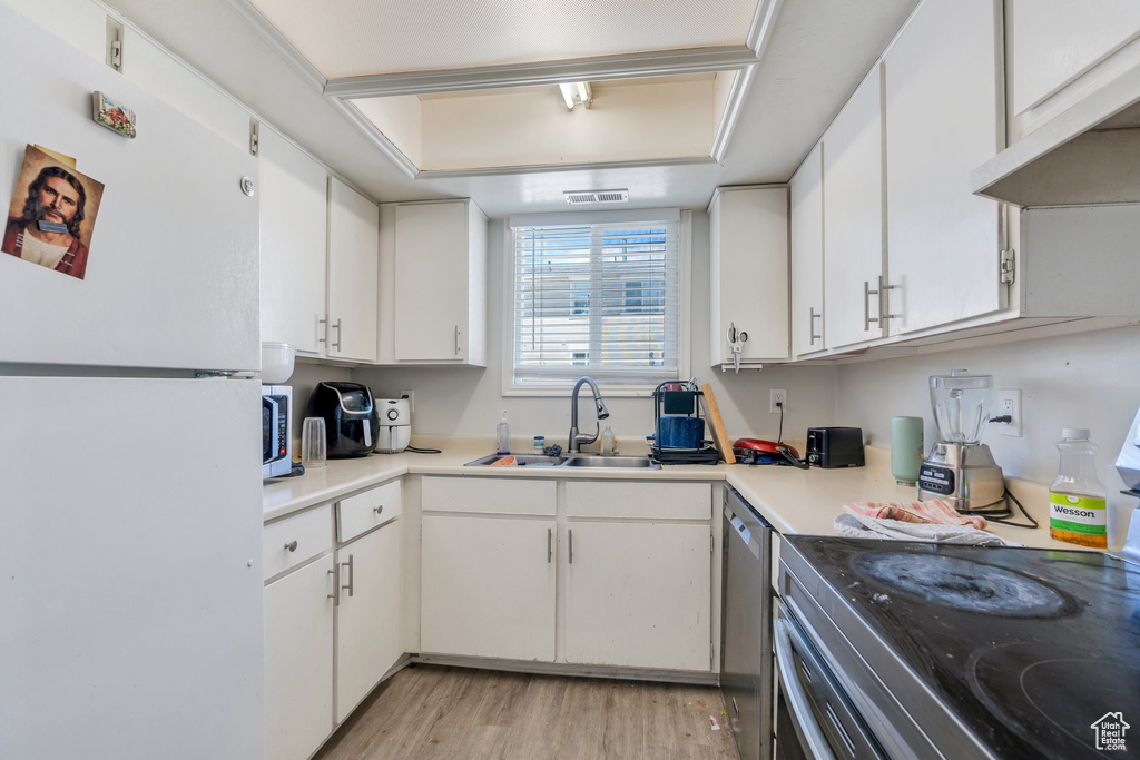 Kitchen with freestanding refrigerator, a sink, light wood finished floors, and white cabinetry