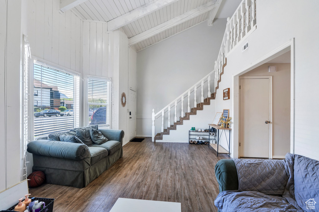 Living area featuring high vaulted ceiling, wood finished floors, beamed ceiling, visible vents, and stairway
