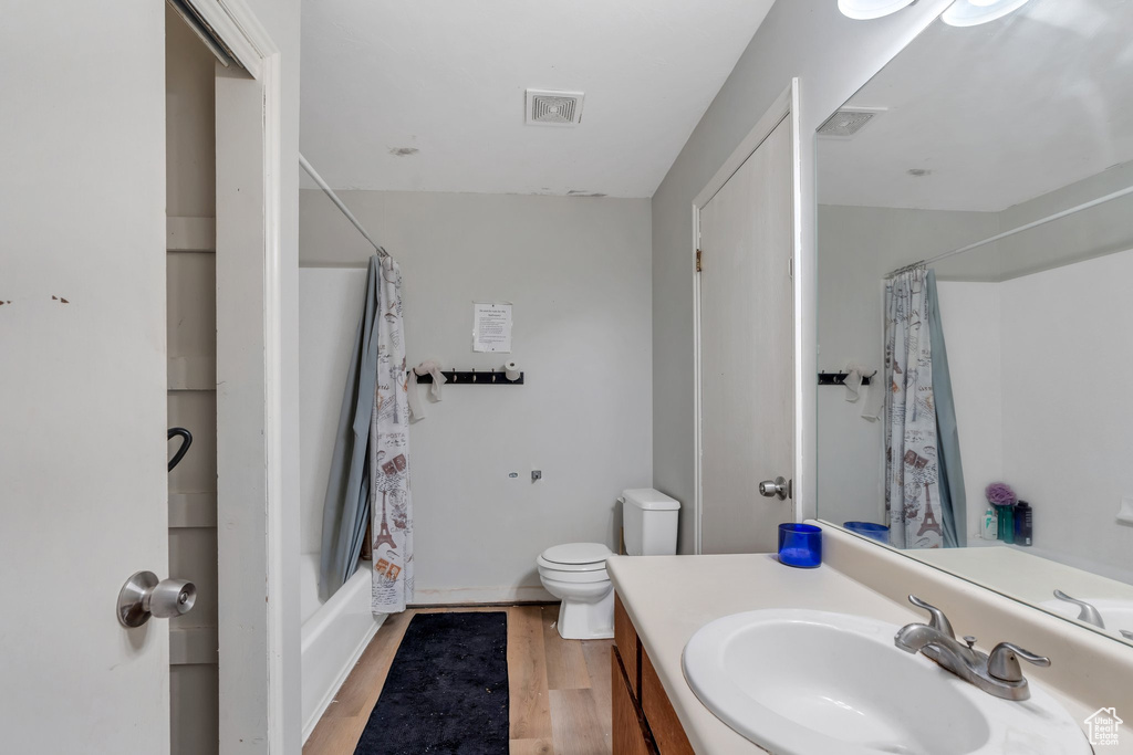 Bathroom featuring visible vents, vanity, wood finished floors, toilet, and shower / bathtub combination with curtain
