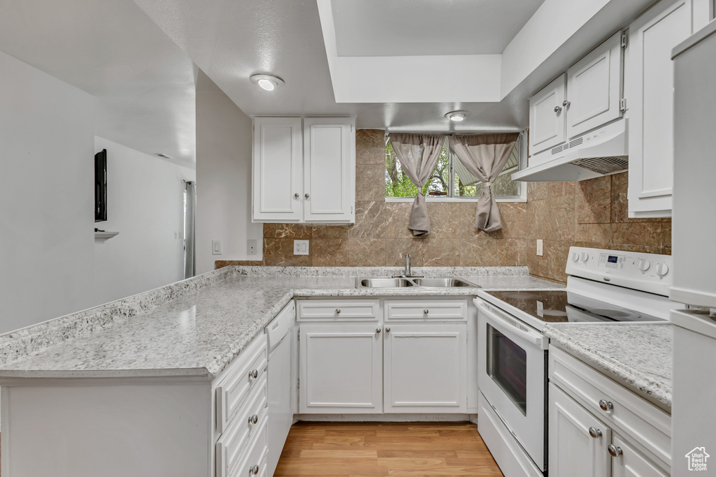 Kitchen with electric stove, under cabinet range hood, a sink, white cabinetry, and a peninsula
