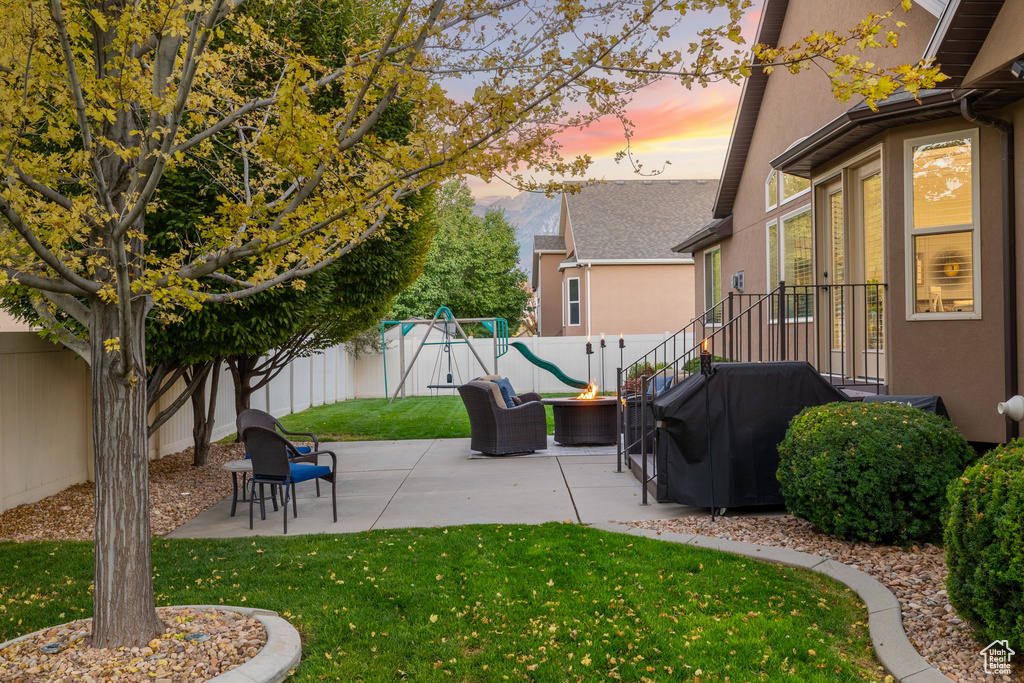 Patio terrace at dusk featuring a lawn, a fenced backyard, outdoor lounge area, and a playground