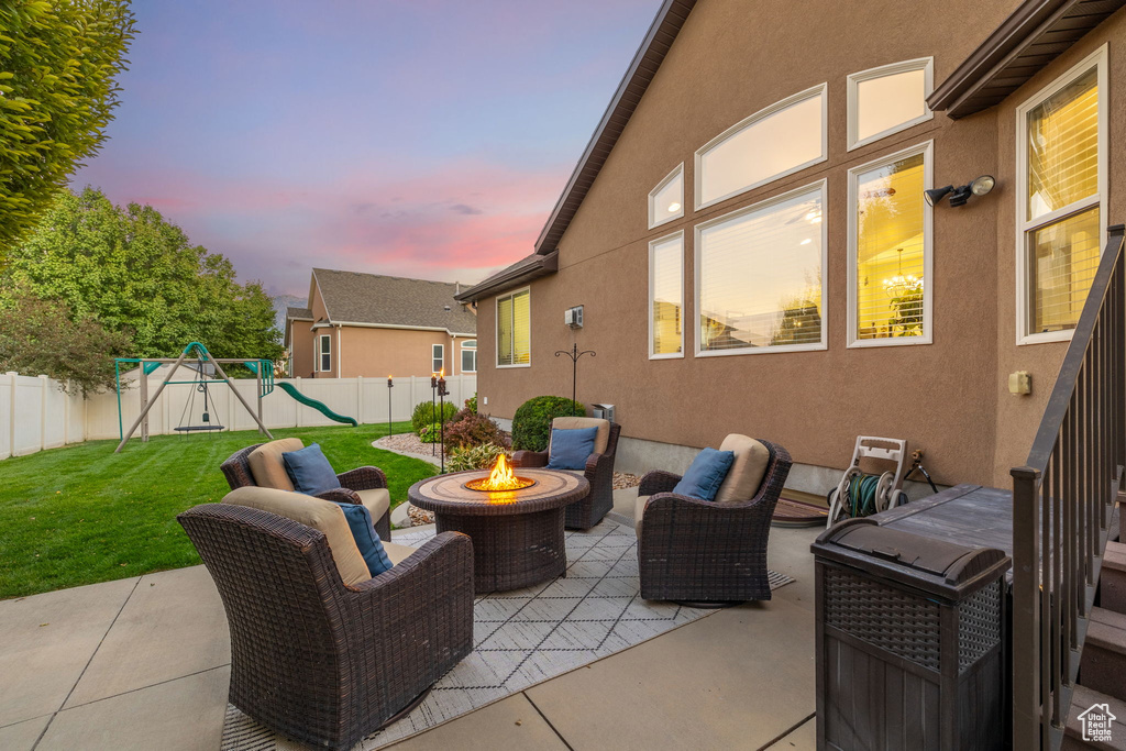 Patio terrace at dusk featuring a fenced backyard, a fire pit, a yard, and a playground