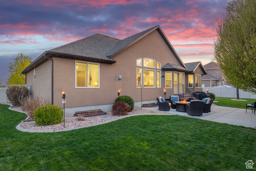 Back of house at dusk with fence, a patio area, and a yard