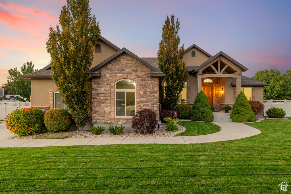 View of front of property with stucco siding, fence, stone siding, and a lawn