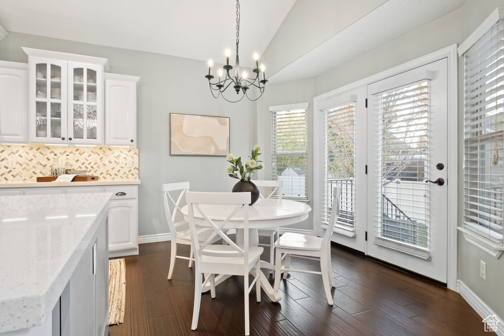 Dining area with vaulted ceiling, a notable chandelier, dark wood-style floors, and baseboards