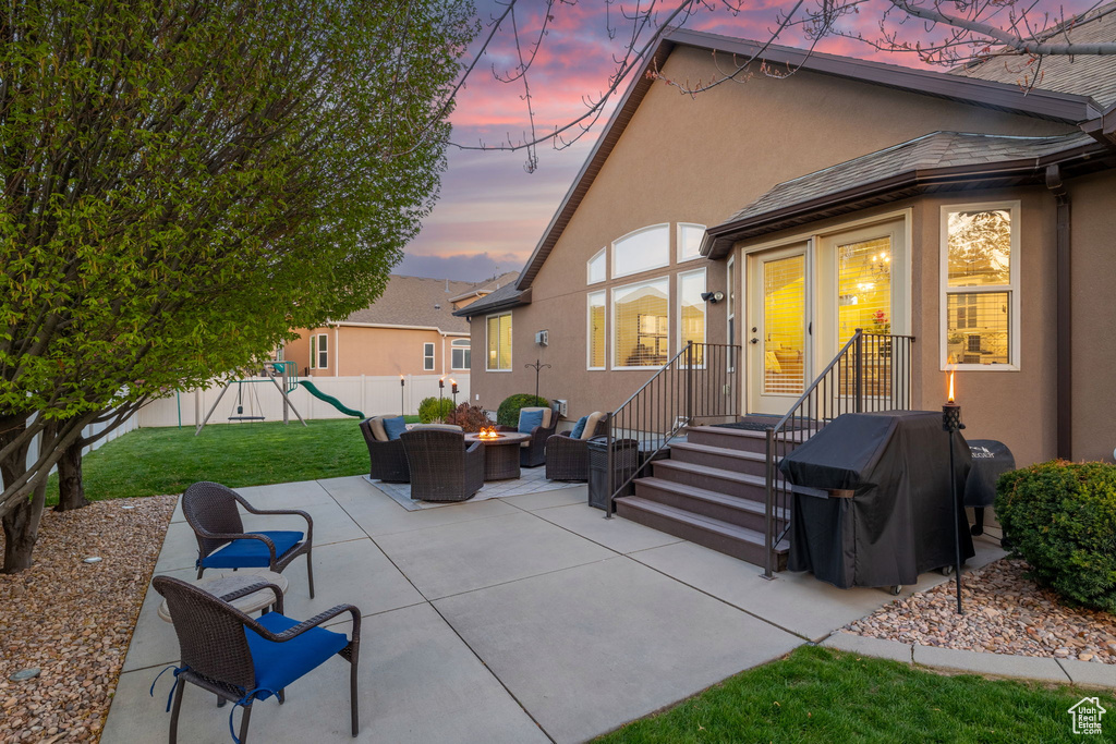Rear view of property featuring a playground, a yard, stucco siding, a patio area, and an outdoor fire pit