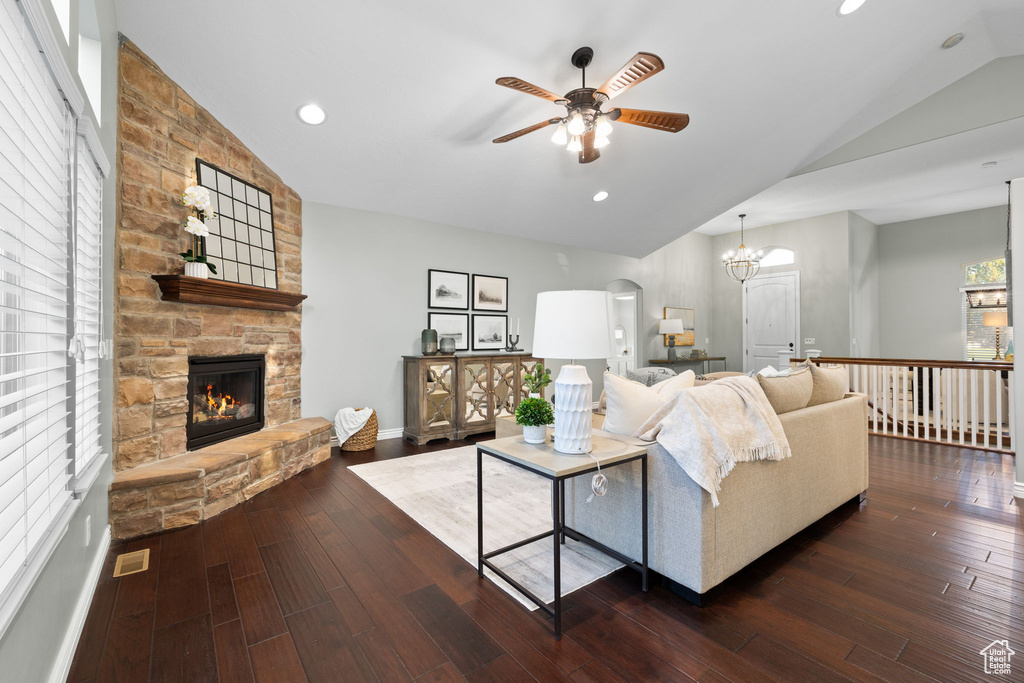 Living room featuring recessed lighting, vaulted ceiling, dark wood-type flooring, a fireplace, and ceiling fan with notable chandelier