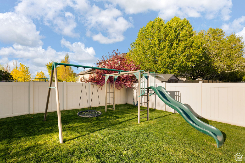 View of play area with a lawn and a fenced backyard
