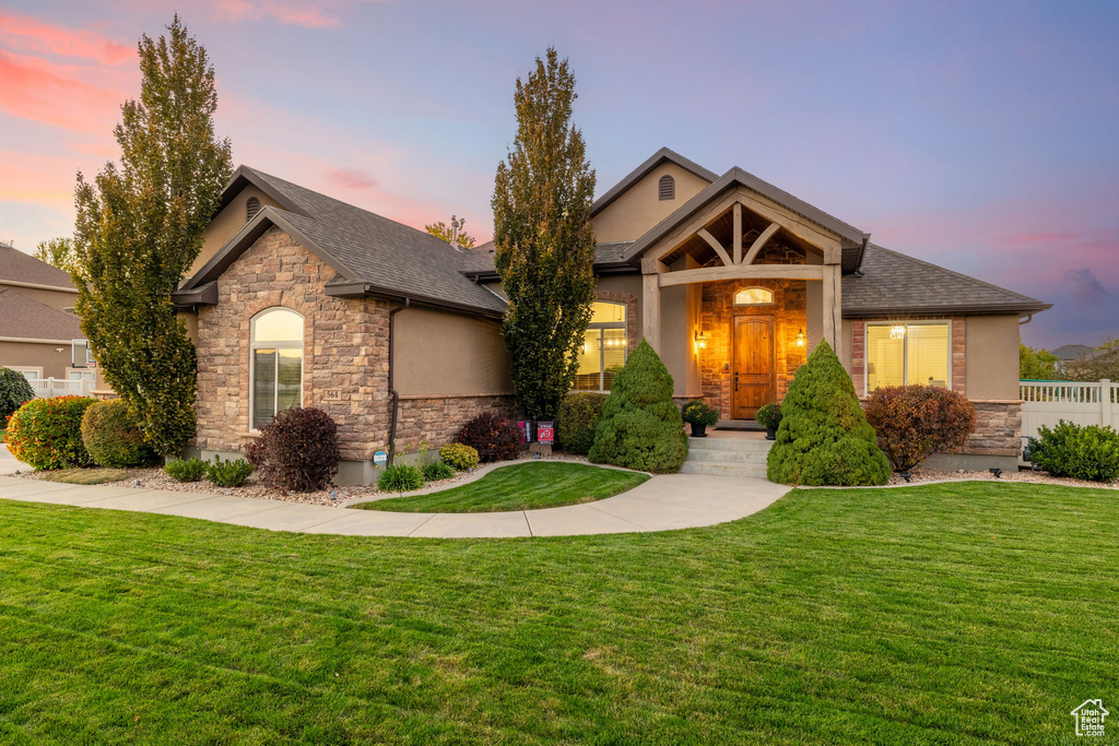 Craftsman-style home with a yard, stone siding, and stucco siding