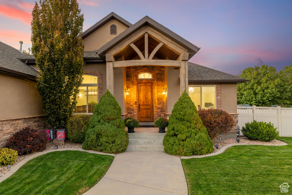 View of exterior entry with stucco siding, a lawn, stone siding, and fence
