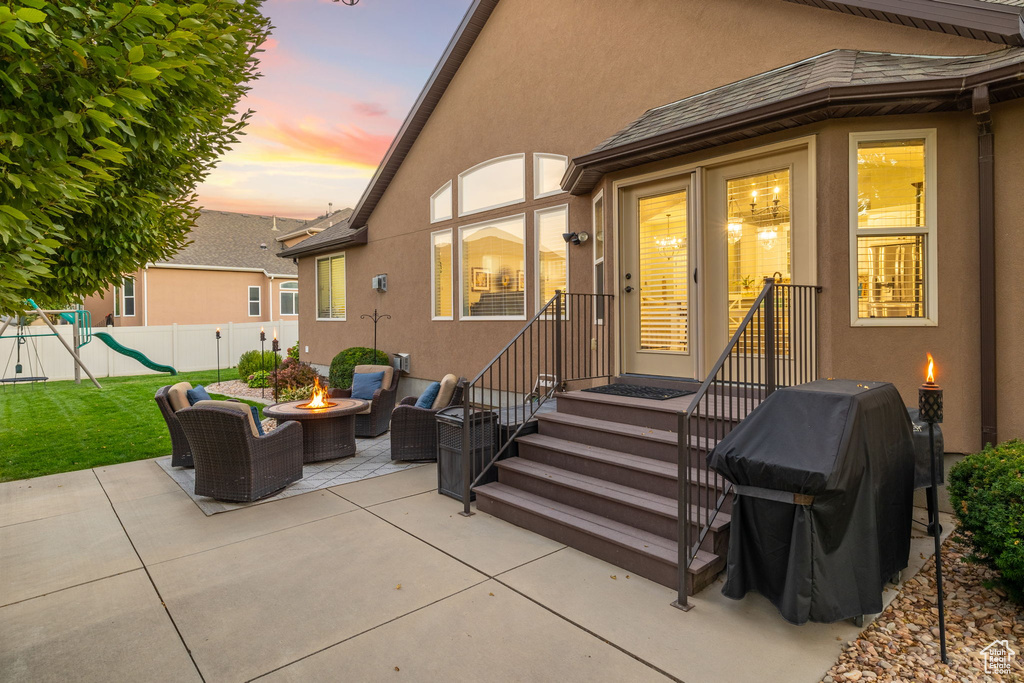Back of house at dusk with a playground, fence, stucco siding, a patio, and a fire pit