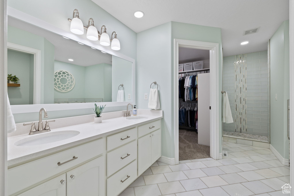 Full bath featuring a tile shower, double vanity, tile patterned flooring, and a sink
