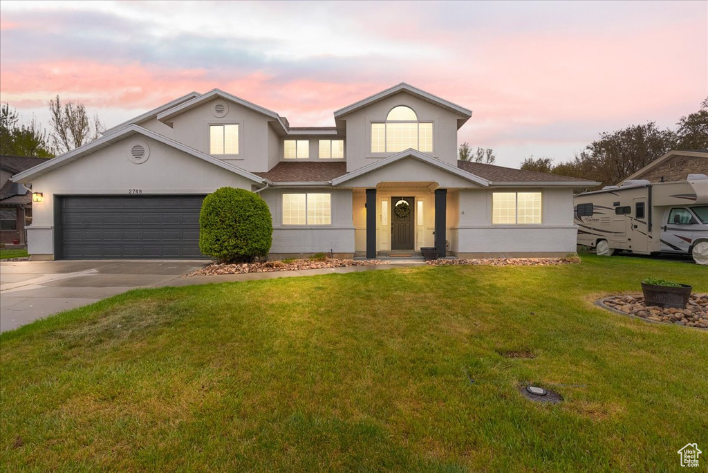 Traditional-style home with roof with shingles, a garage, stucco siding, a front yard, and driveway