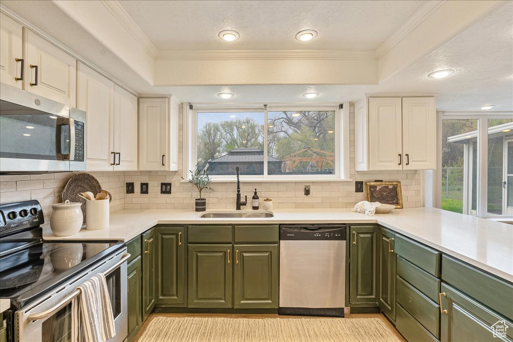 Kitchen featuring decorative backsplash, a sink, green cabinetry, stainless steel appliances, and white cabinetry