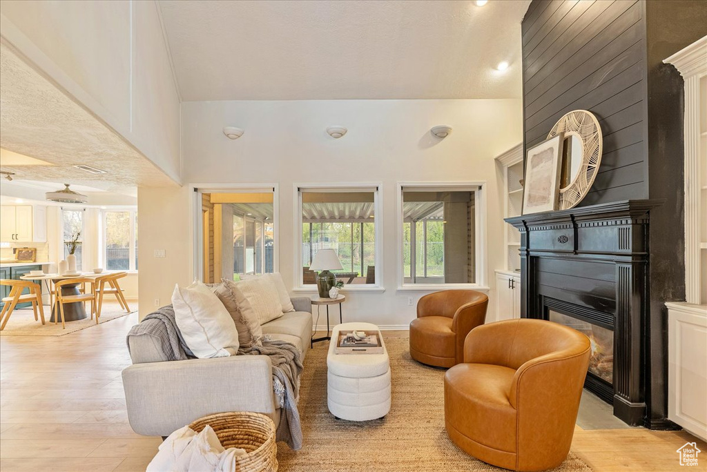 Living area with a glass covered fireplace, plenty of natural light, light wood-style flooring, and a towering ceiling