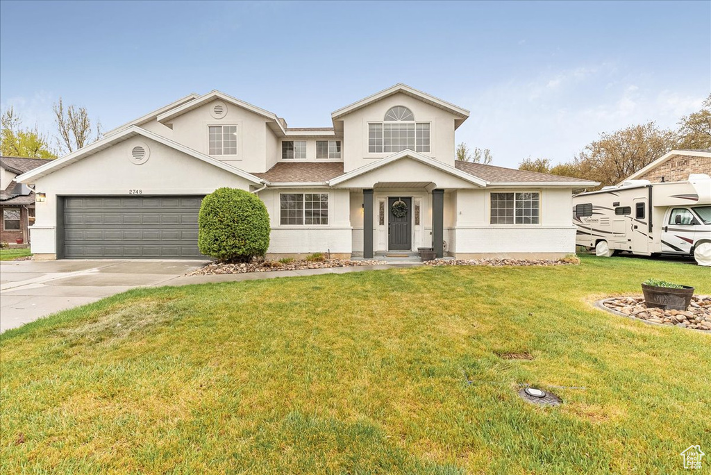 Traditional-style home featuring roof with shingles, a front lawn, a garage, stucco siding, and concrete driveway