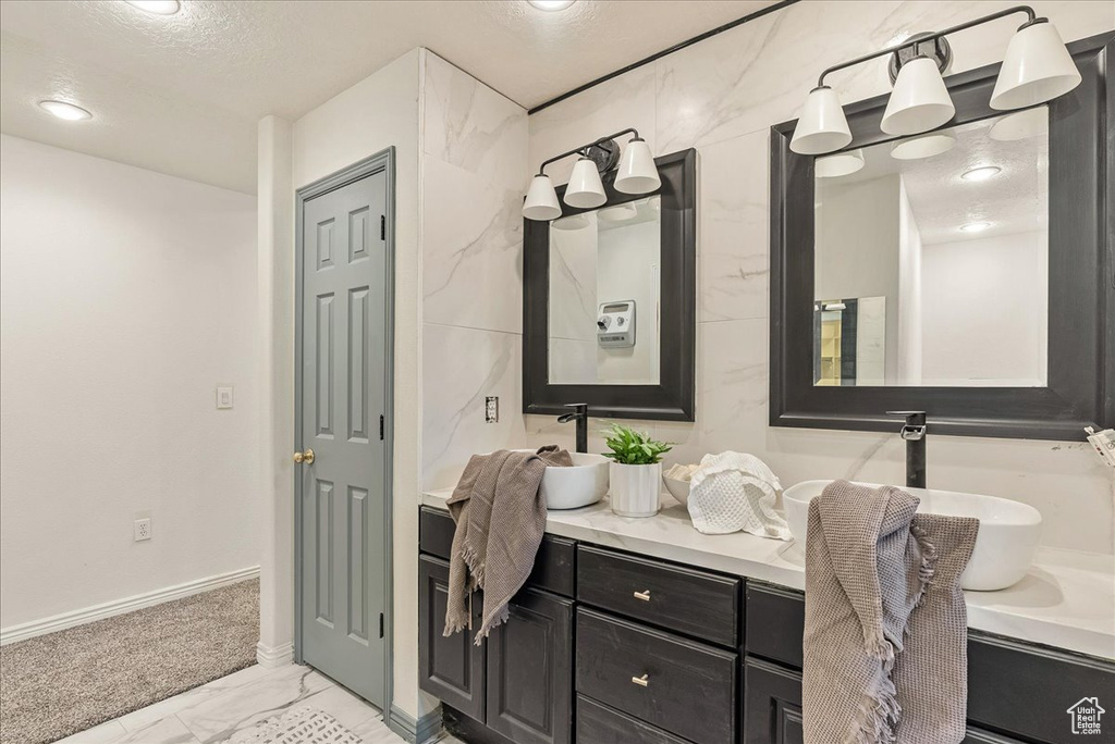 Bathroom featuring double vanity, marble finish floor, baseboards, a textured ceiling, and a sink