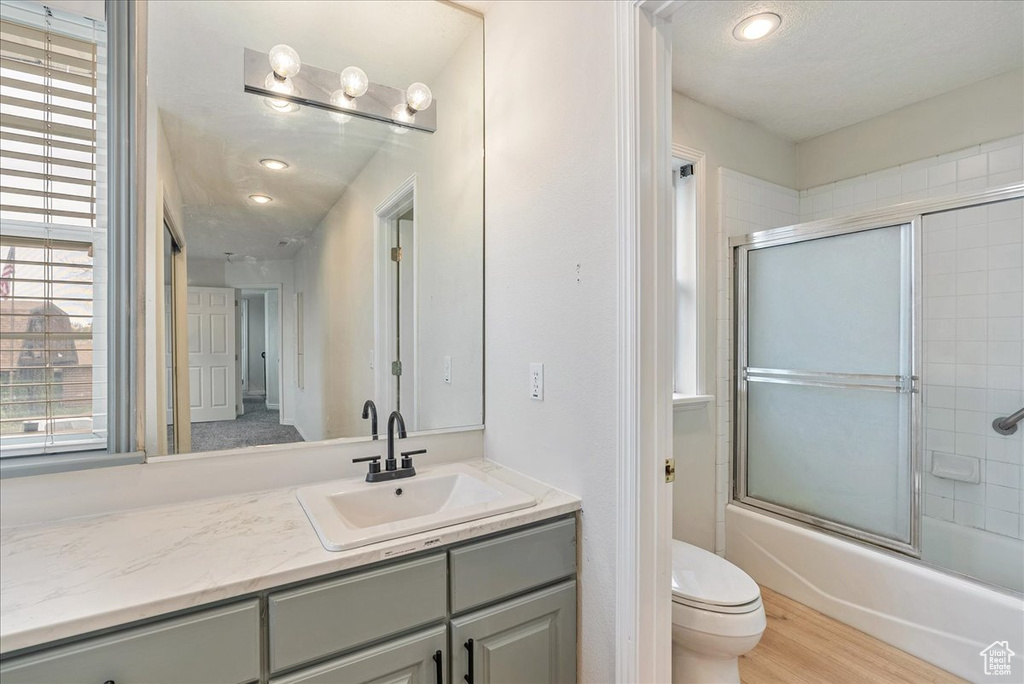 Bathroom featuring vanity, wood finished floors, toilet, recessed lighting, and combined bath / shower with glass door