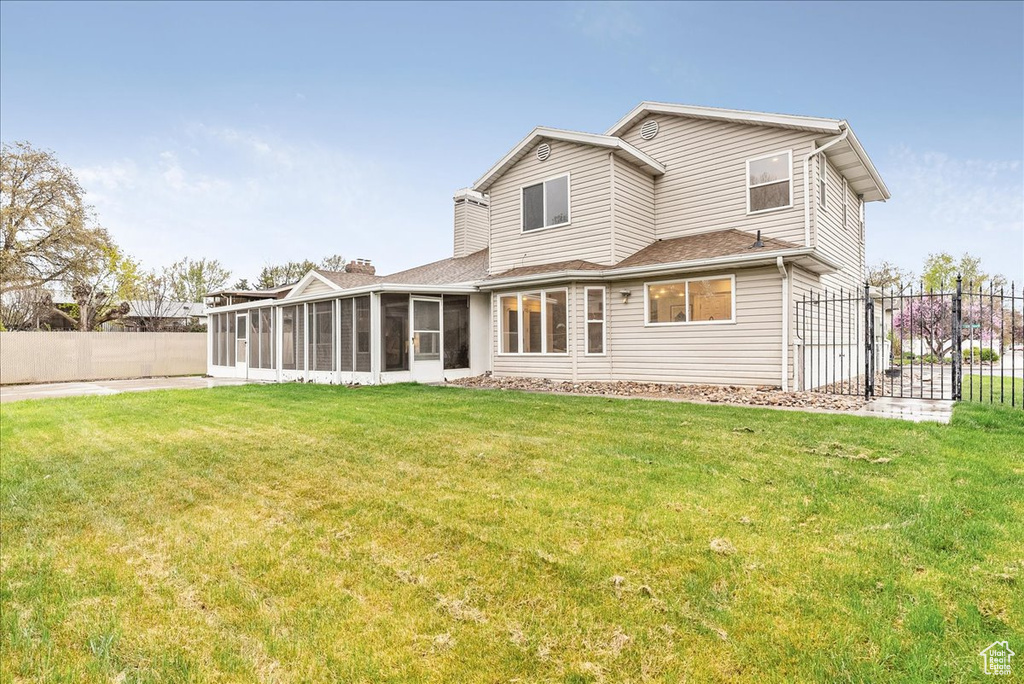 Back of property featuring a chimney, a lawn, a gate, a sunroom, and fence
