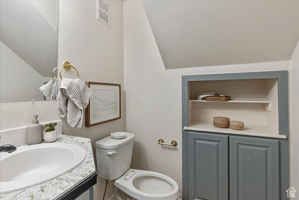 Half bath featuring toilet, visible vents, lofted ceiling, and vanity