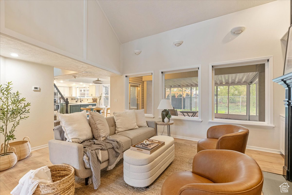Living room featuring stairway, high vaulted ceiling, baseboards, and light wood finished floors