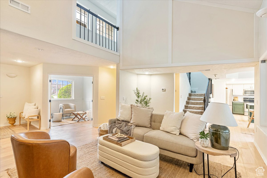 Living room featuring a high ceiling, light wood-style flooring, baseboards, visible vents, and stairway