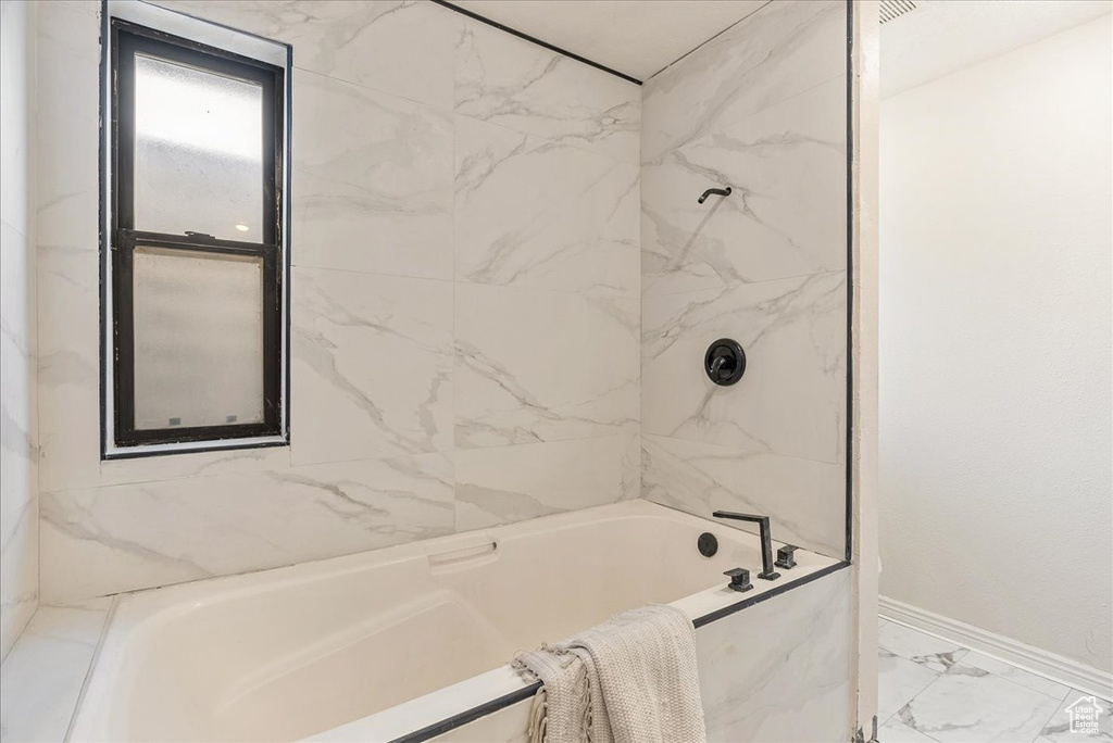 Bathroom featuring baseboards, marble finish floor, and washtub / shower combination