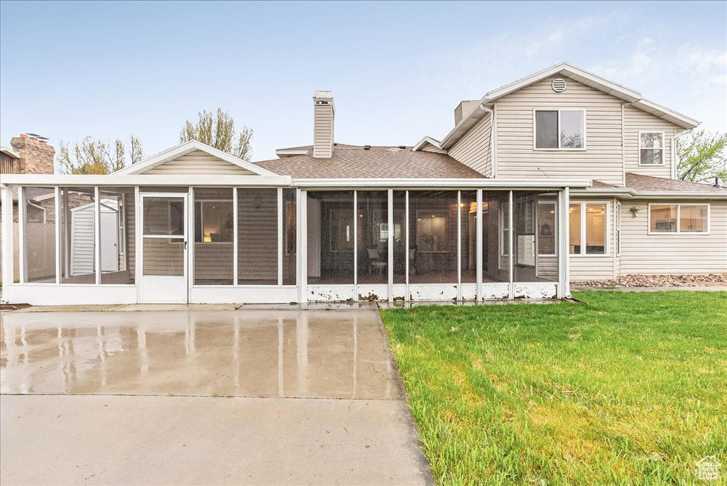Back of property with a sunroom, a lawn, roof with shingles, and a chimney